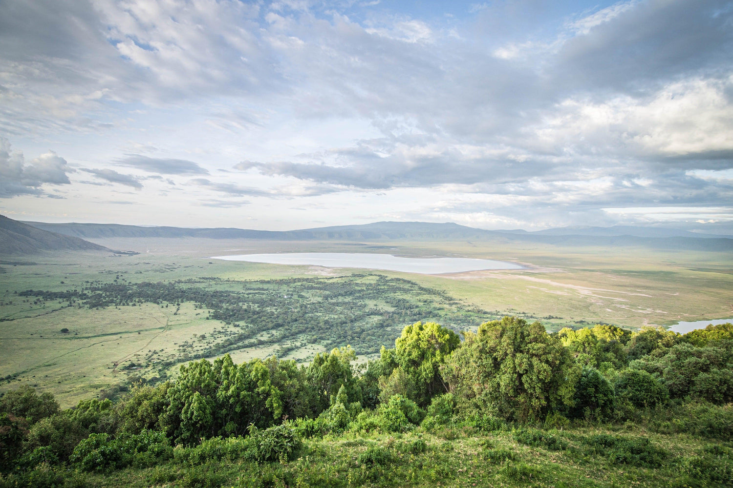 Fine Ngorongoro Crater photography print of the expansive crater atop the rim as the clouds breach the crater, casting shadows on the luscious landscape.