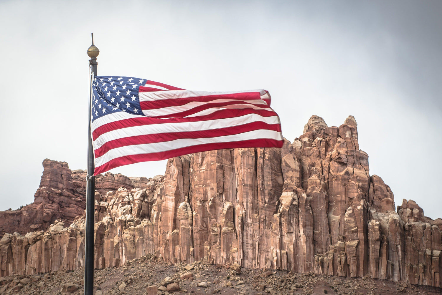 Fine Capitol Reef National Park photography print of an American flag blowing in the wind with rock formations in the background.