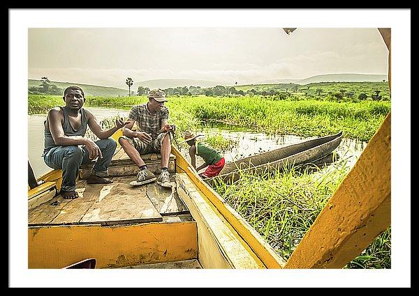 Framed fine photographic and art print of three Congolese men operating a wooden boat and small wooden canoe along the Congo River during the day in the Democratic Republic of the Congo.