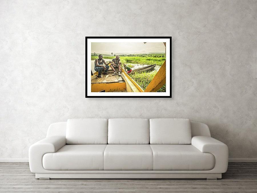 Framed fine photographic and wall art print of three Congolese men operating a wooden boat and small wooden canoe along the Congo River during the day in the Democratic Republic of the Congo.
