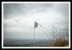 Framed fine photographic and art print of a ripped Democratic Republic of the Congo flag on top of a mountain overlooking a small village. 