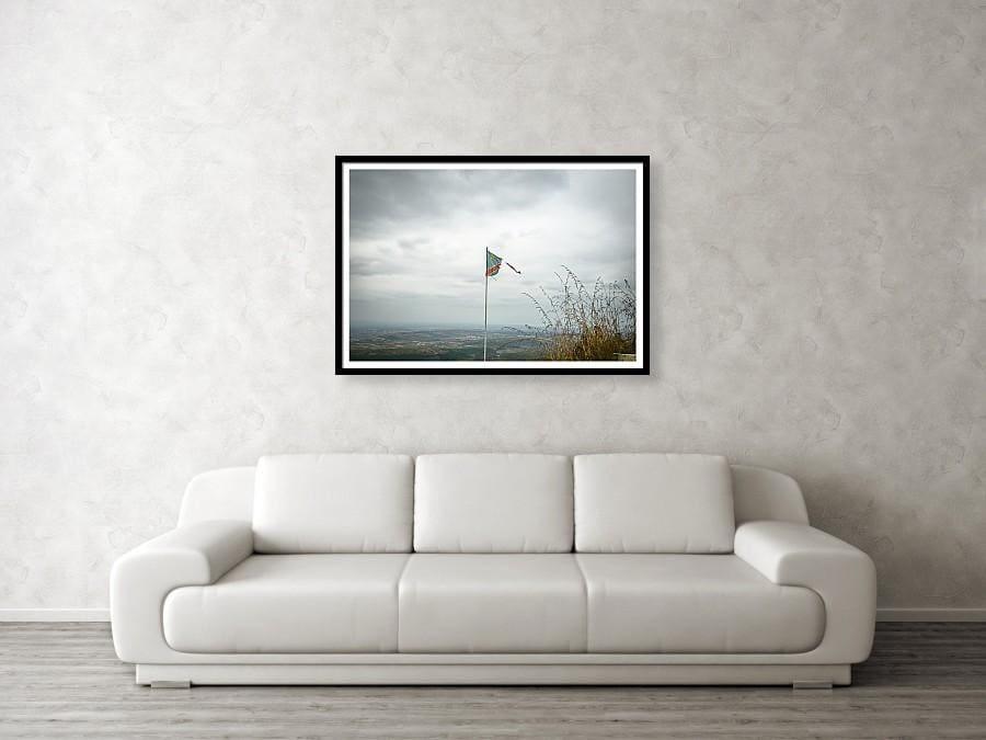 Framed fine photographic and wall art print of a ripped Democratic Republic of the Congo flag on top of a mountain overlooking a small village. 
