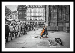 Framed fine black and white photographic and art print of a solo colorful cellist playing outside the doors of Strasbourg Cathedral as Christmas crowds gather and listen as they wait to enter.